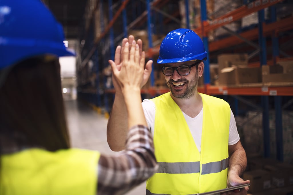 Warehouse worker giving high five to his friend colleague.